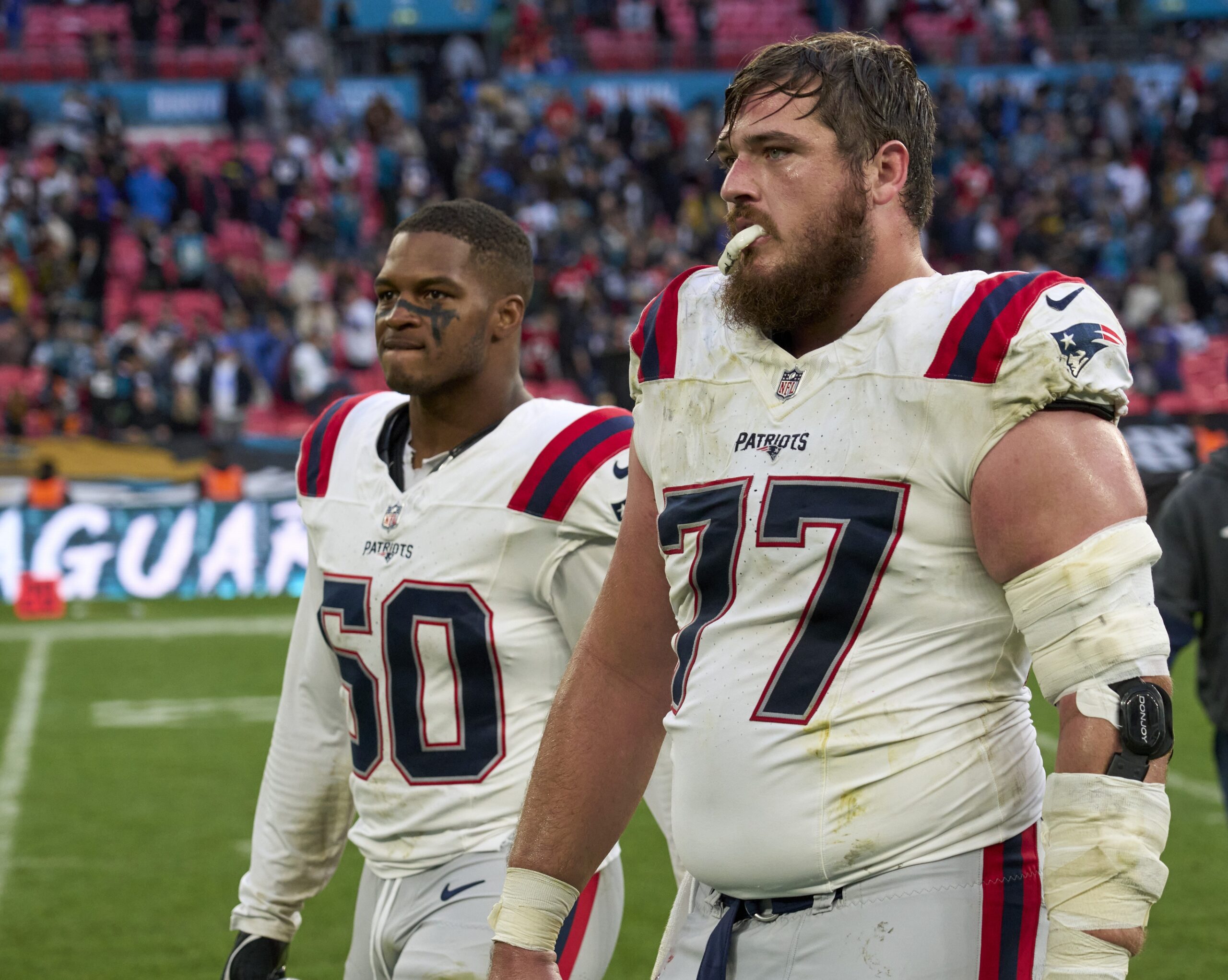 Oct 20, 2024; London, United Kingdom; New England Patriots center Ben Brown (77) and New England Patriots linebacker Raekwon McMillan (50) eave the field after an NFL International Series game at Wembley Stadium. Mandatory Credit: Peter van den Berg-Imagn Images