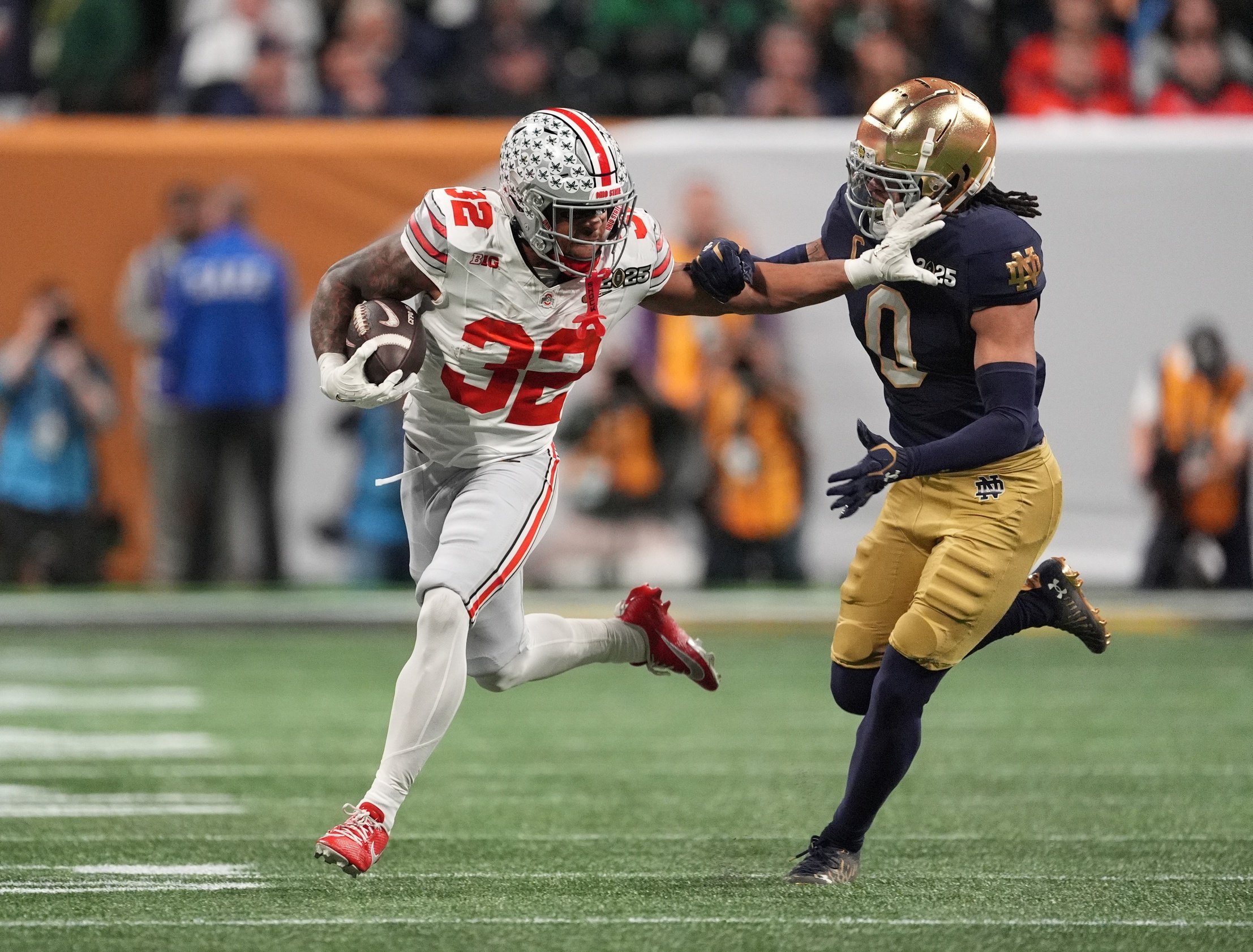 Jan 20, 2025; Atlanta, GA, USA; Ohio State Buckeyes running back TreVeyon Henderson (32) stiff arms Notre Dame Fighting Irish safety Xavier Watts (0) in the first half in the CFP National Championship college football game at Mercedes-Benz Stadium. Mandatory Credit: Dale Zanine-Imagn Images